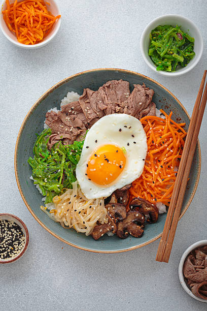 Traditional korean bibimbap with fried egg, beef and vegetables and other toppings top view on light background