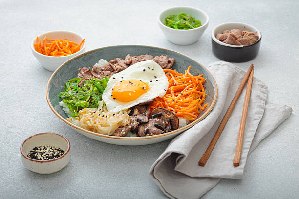Traditional korean bibimbap with fried egg, beef and vegetables and other toppings on light background with chopsticks