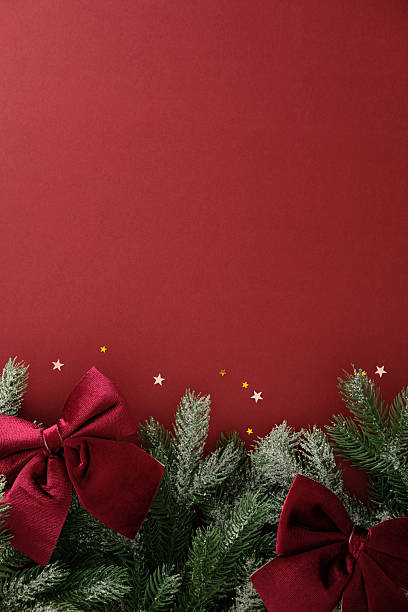 istock Snowy pine branches with red bows and star confetti on a deep red background. Christmas, New Year, winter holidays vertical background. 2243470043
