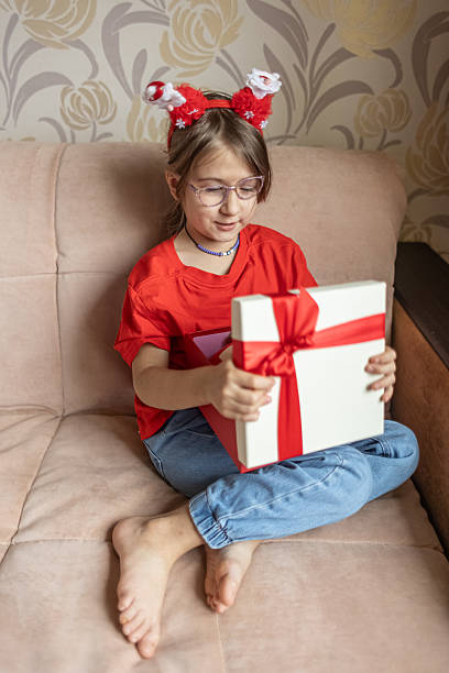 istock A girl in a Santa Claus hat opens a gift. It's Christmas time. 2243470103