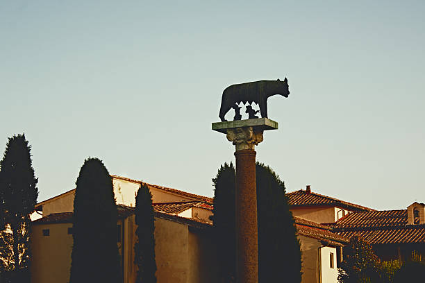 Close-up of column with stone block topped by she-wolf nursing Romulus and Remus, warm golden tones, Italian heritage, sculpted mythological detail, historical architecture, Tuscany.