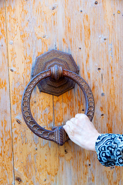 istock Rustic Wooden Door With Iron Ring Knocker And Hand Grasping It 2243478850