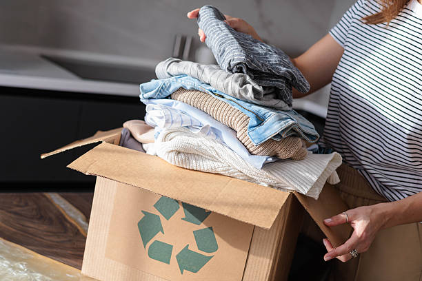 istock Female hands put clothes to recycling zero waste reusing cardboard box on table at home closeup. 2243481203
