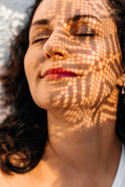 istock Woman's face with closed eyes, red lips, leaf shadow pattern in sunlight, peaceful moment 2243481337