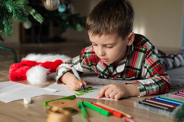 istock Child drawing Christmas tree on paper lying on floor under festive decorated holiday tree 2243481664