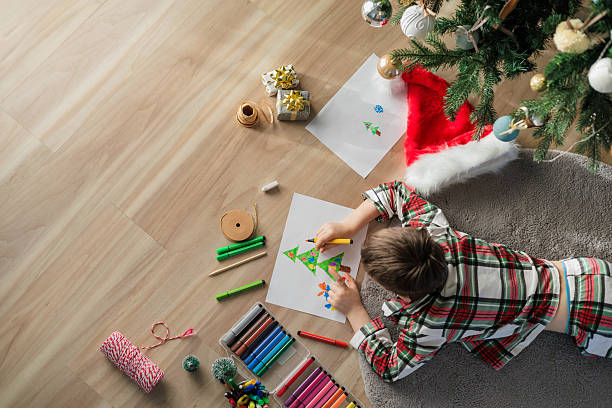istock Child drawing Christmas tree lying under decorated tree in festive red green pajamas 2243481699