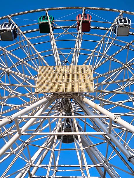 istock A giant Ferris wheel with multi-colored enclosed cabins against a clear sky. 2243486329
