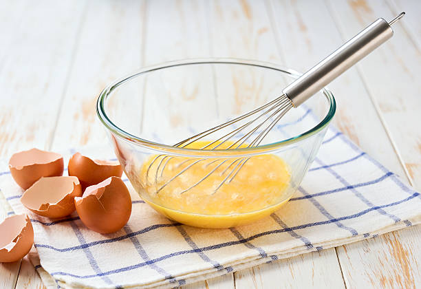 istock beat eggs with egg whisk in a glass bowl on a kitchen table. Cooking scrambled fresh eggs for breakfast. 2243487021