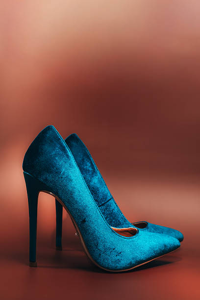A pair of blue high heels with a shiny, glittery surface. The shoes are placed on a red background, which creates a striking contrast between the bright blue and the warm red tones