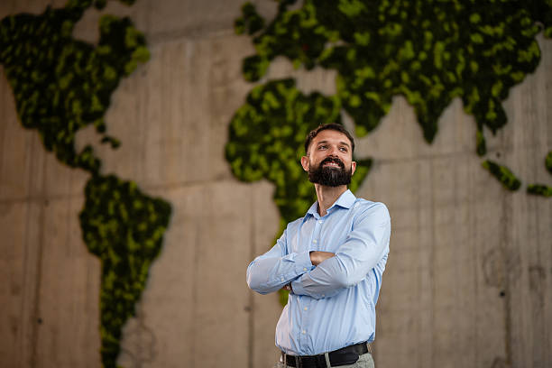 istock Businessman standing with arms crossed next to world map 2243489221