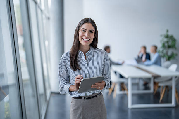 istock Smiling businesswoman using digital tablet in modern office with team working in background 2243493370
