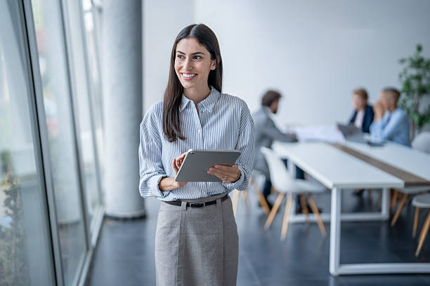 istock Smiling businesswoman using digital tablet in modern office with colleagues working in background 2243493375
