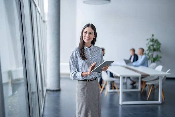 istock Young businesswoman using digital tablet in modern office with colleagues in background 2243493376