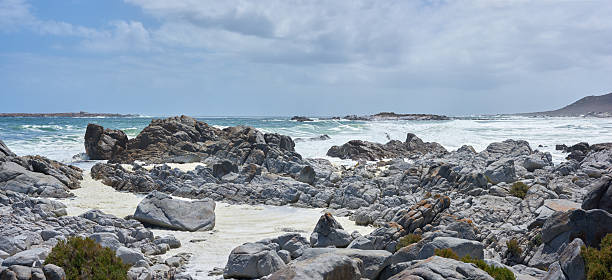 A scenic lookout over a rugged coastal shoreline featuring enigmatic grey rock formations and foamy ocean waves beneath a cloud-filled sky. A view embodying the raw, unfiltered splendor of natural marine landscapes.