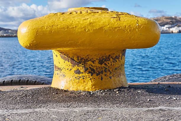 A vibrant yellow mooring bollard is situated on a dock overlooking the calm waters and distant coastal landscape, reflecting Norwegian maritime heritage and functionality, bathed in natural light, creating a vivid visual contrast.