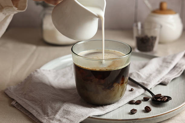 istock Woman pouring milk into cup with coffee at light table, closeup 2243510286