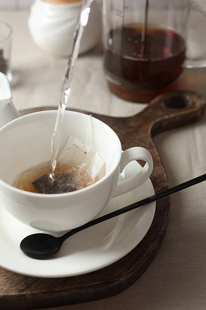istock Pouring hot water into cup with tea bag on light table, closeup 2243510317