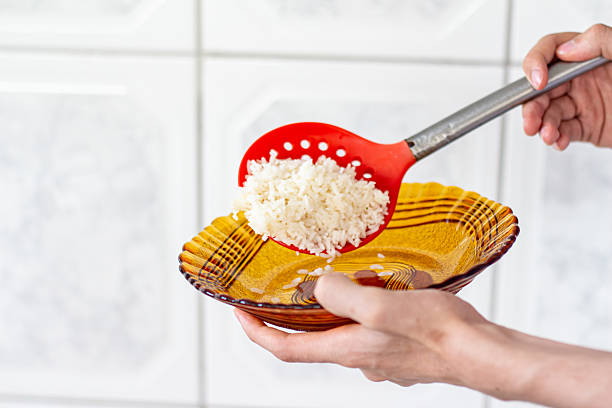 Serving cooked white rice with a red spoon into an amber glass plate in kitchen.
