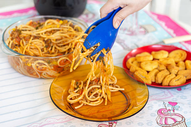 Serving hot spaghetti with meat sauce using blue tongs, home-cooked meal.