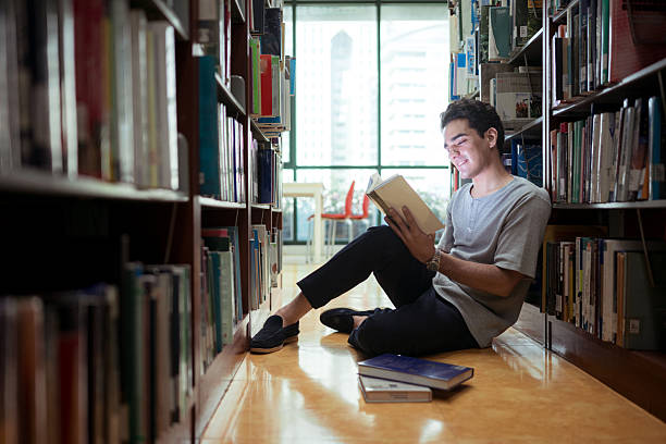 istock A young man sitting on the library floor reading a book with concentration 2243516724