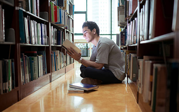 istock A young man sitting on the library floor reading a book with concentration 2243516741