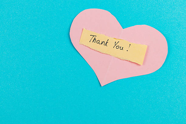 A pink heart cutout features a yellow note that says thank you. The heart is placed on a bright blue background, creating a cheerful and uplifting vibe.