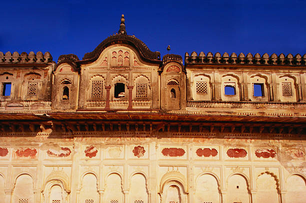 Grand gateway with Mughal architecture, characterized by its towering minarets and intricate red sandstone and white marble inlay. The structure features a large central arch flanked by smaller arches, adorned with geometric and floral patterns. The four minarets rise symmetrically, adding to its majestic appearance. The architectural style reflects a blend of Islamic, Persian, and Indian influences, typical of the Mughal era. The overcast sky enhances the monument s striking detail and symmetry.
