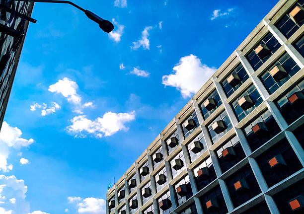 A low-angle shot captures the repetitive, geometric facade of a modern building against a vibrant blue sky with scattered clouds.