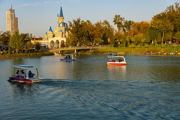 Tashkent, Uzbekistan, October 18, 2025: Scenic lake with pedal boats and a whimsical castle-like building in the background, blending leisure, nature, and urban charm