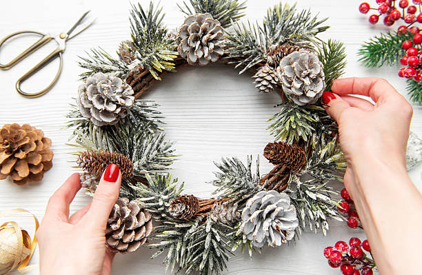 istock Hands decorating christmas wreath with pine cones and evergreen 2243539503
