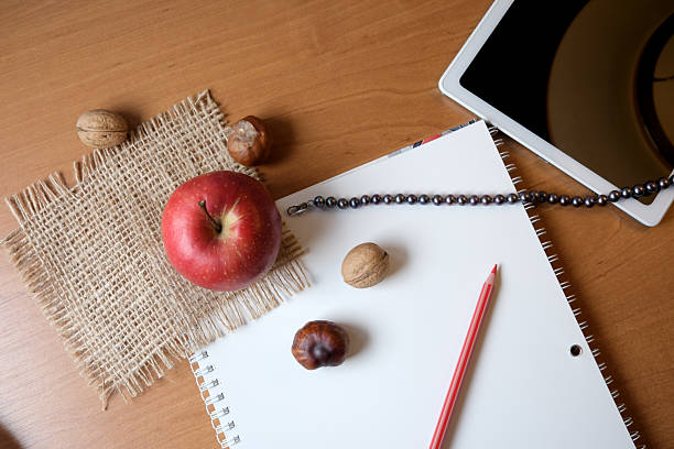 A cozy workspace features an apple, nuts, and a blank notebook ready for notes.