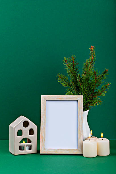 istock Decorative arrangement with empty frame, candles, and greenery on green background for mock up 2243543753