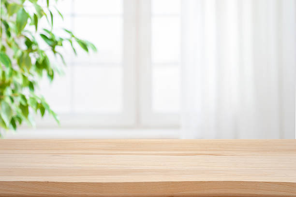 istock Empty wooden table against blurred window with curtain and green pant branch background 2243543982