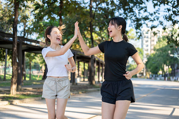 istock Pretty asian woman clapping hands high five a friend while running jogging on concrete road in park. 2243545333