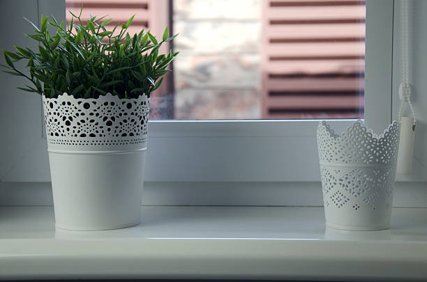 Plastic tulips in a tall white plastic vase placed on a white table by the window. Venetian Aluminum Blinds pattern on the background.