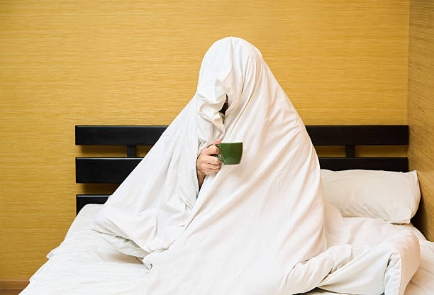 istock Man wrapping in blanket sitting with cup of coffee in bed 2243548863