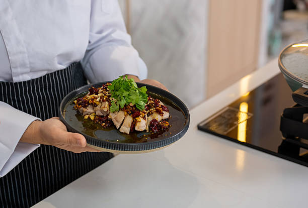 An Asian Chinese chef holds a spicy chicken dish before serving it in a professional kitchen