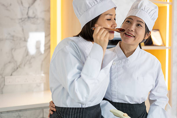 Two Chinese women chefs taste a spicy chicken dish before serving it in a busy commercial kitchen
