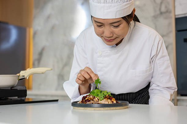 An Asian Chinese chef adds the final touches to a plate of spicy chicken in a professional kitchen before serving