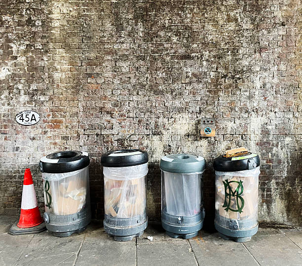 Four public litter bins, a traffic cone, and a plaque with the number 45A on a damp brick wall in arches under a railway track.