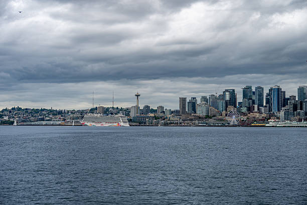 A colorful cruise ship is docked along the Seattle waterfront with the iconic Space Needle rising in the background. Captured under a cloudy sky, the image highlights maritime travel, city infrastructure, and Pacific Northwest landmarks.