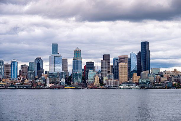 A dramatic view of downtown Seattle, Washington, captured from across Puget Sound under heavy clouds. The modern skyline features iconic skyscrapers and waterfront buildings, illustrating the city’s urban density and architectural diversity.