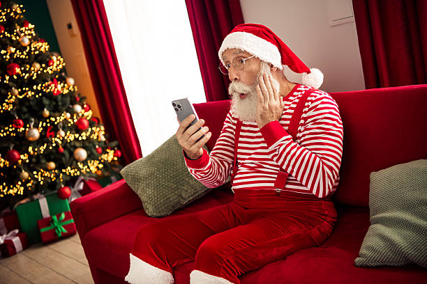 istock Santa Claus wearing a red striped outfit surprised while using a smartphone during Christmas season in a cozy home 2243571138
