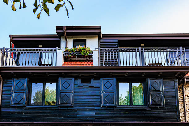 Charming wooden house facade with balcony and greenery under clear sky.