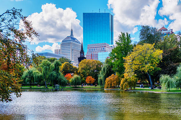 Boston, Massachusetts, USA - October 25, 2025: View across the Boston Public Garden pond of Boston's Back Bay neighborhood skyline. Prominent Back Bay buildings include the Arlington Street Church; the Berkeley Building, also known as the Old John Hancock building, with its distinctive weather beacon at its summit; 200 Clarendon Street skyscraper (aka John Hancock Tower); and the Prudential Center skyscraper.  Established in 1837, the Public Garden is a large park in the heart of Boston, adjacent to Boston Common. It is a part of the Emerald Necklace system of parks. The Public Garden was the first public botanical garden in America.
