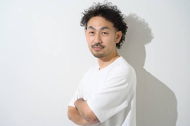 A Japanese man wearing short sleeves with arms crossed on a white background