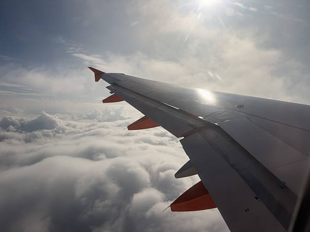 istock Airplane wing flying above clouds with sun flare 2243582565