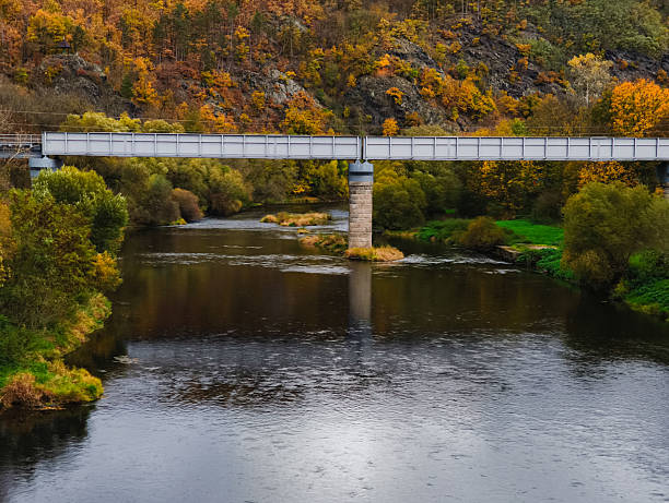 Roztoky u Krivoklatu, Czech republic - October 25, 2025: Berounka river flowing under a metal railway bridge, surrounded by colorful autumn trees