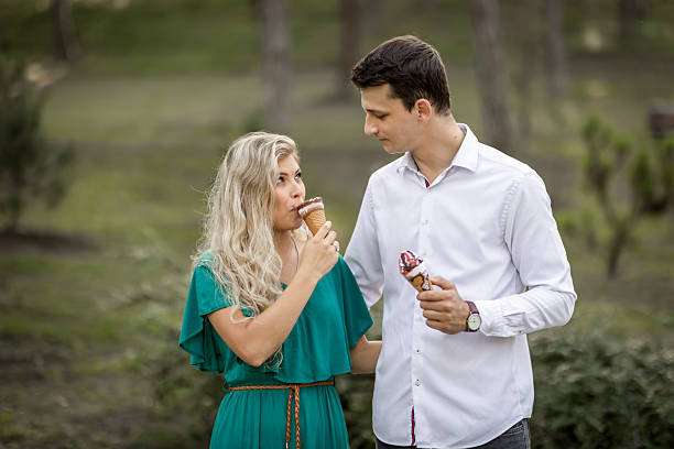 Smiling couple walking hand in hand through a park while enjoying ice cream cones on a warm day. Perfect image for concepts of love, romance, summer lifestyle, togetherness, and carefree happiness.