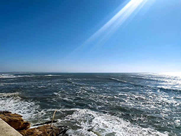 istock A dramatic seascape featuring the ocean under a clear blue sky and bright sunlight. Waves crash against rocks, creating sea foam. Ideal for travel, nature, or inspirational themes. 2243587713